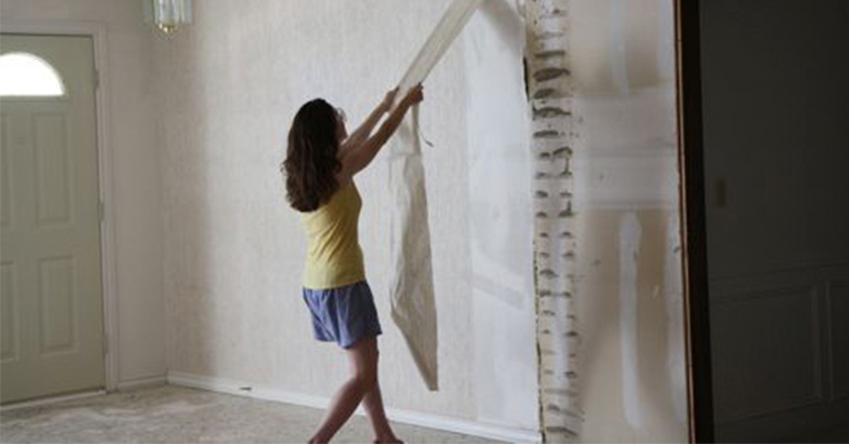 A girl is removing old wallpaper